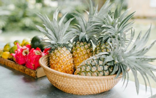 Fresh tropical fruit display featuring ripe pineapples and dragon fruit in a woven basket. Ideal for restaurant websites, organic food blogs, and travel articles focusing on Southeast Asian cuisine